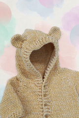 Círculo Amigurumi Pelúcia – Polyester Chenille Yarn (131 m / 85 g) - A close-up of a beige chunky knit hooded cardigan with bear ears on the hood and front buttons, shown against a pastel watercolor background.