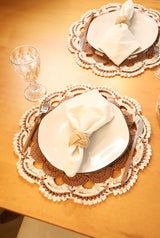 Círculo Natural Cotton Multicolor 4/6 – Cotton Yarn (226 m / 200 g) – A styled table setting featuring round white plates on brown and cream crocheted lace placemats, with a folded cream napkin tied in a knot and silver cutlery, on a warm wooden table.