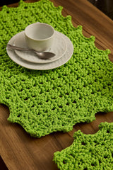 Circulo Fio Náutico Poly 5 mm – Polyester Cord Yarn ( 178 m  / 500 g) - A bright lime green crocheted placemat with an irregular scalloped edge, styled on a wooden table with a white ceramic cup and saucer and a spoon.